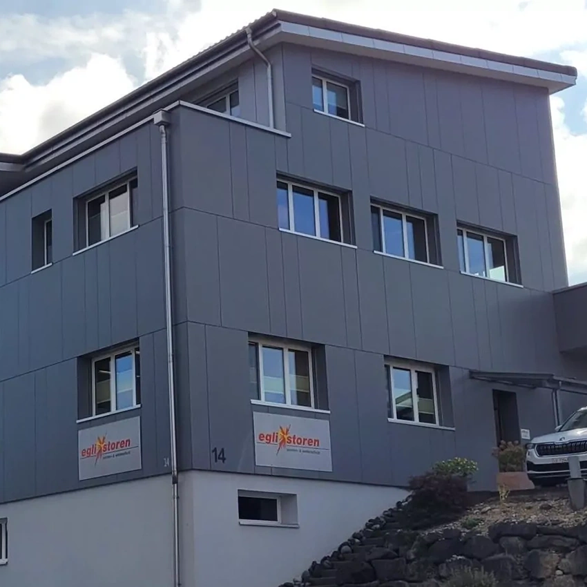 Dunkelgraues, modernes Firmengebäude der Egli Storen AG, auf dem ein Schild mit deren Logo zu sehen ist.