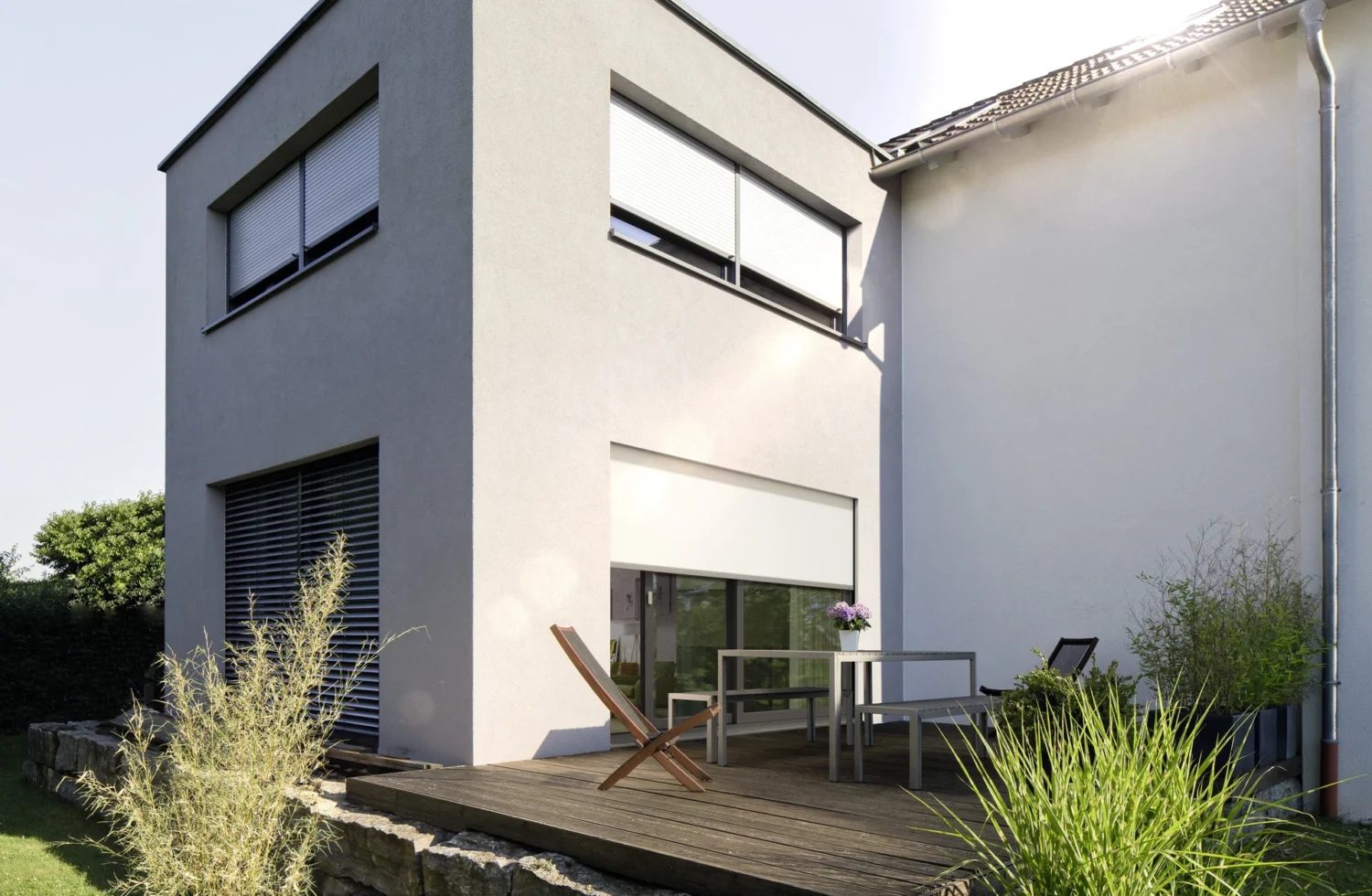 Moderne Terrasse mit Holzdeck und Gartenmöbeln vor einem zweistöckigen Wohnhaus